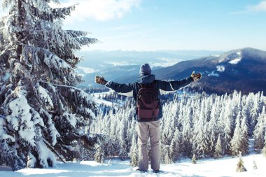 Sırt çantalı mutlu bir adam dağlarda yürüyüş yapıyor. Dağların tepesinde bir yürüyüşçü. Soğuk hava, tepelerde kar. Kış yürüyüşü. Seyahat, dinlenme, rahatlama ve spor yaşam tarzı kavramı.