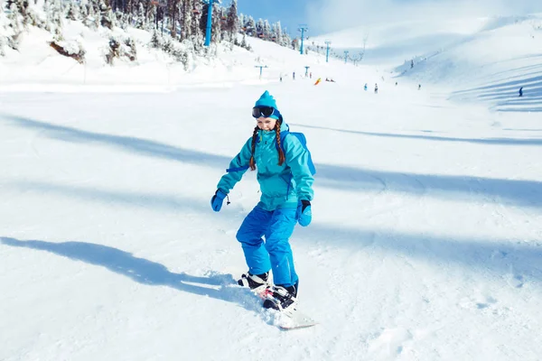 滑雪板女孩 一个穿着冬衣的漂亮姑娘正骑着雪板 她戴着蓝色头盔和一件夹克 冒险参加冬季运动 体育的概念 — 图库照片