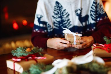 Erkeklerin elleri kırmızı kurdeleli hediye kutusunu tutuyor. Noel şenliği ruhu. Adam bunu kendisi yaptı ve bayram için verecek. Yeni yıl hediyesi. Şömineli güzel bir arkaplan.