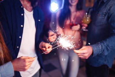 Bir grup mutlu insan partide maytap tutuyor ve gülümsüyor. Gençler yeni yılı birlikte kutluyor. Arkadaşlar maytapları yaktı. Arkadaşlar akşamları havai fişeklerle eğleniyorlar. Bulanık Arkaplan.