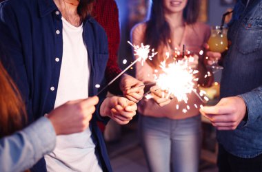 Bir grup mutlu insan partide maytap tutuyor ve gülümsüyor. Gençler yeni yılı birlikte kutluyor. Arkadaşlar maytapları yaktı. Arkadaşlar akşamları havai fişeklerle eğleniyorlar. Bulanık Arkaplan.
