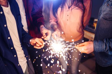 Bir grup mutlu insan partide maytap tutuyor ve gülümsüyor. Gençler yeni yılı birlikte kutluyor. Arkadaşlar maytapları yaktı. Arkadaşlar akşamları havai fişeklerle eğleniyorlar. Bulanık Arkaplan.