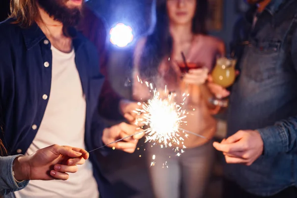 Group of happy people holding sparklers at party and smiling.Young people celebrating New Year together. Friends lit sparklers. Friends enjoying with sparklers in evening. Blur Background.