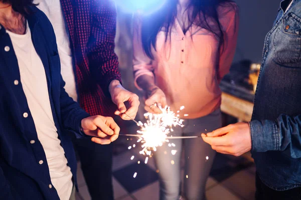 Group of happy people holding sparklers at party and smiling.Young people celebrating New Year together. Friends lit sparklers. Friends enjoying with sparklers in evening. Blur Background.