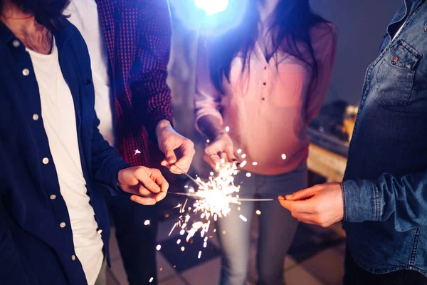 Group of happy people holding sparklers at party and smiling.Young people celebrating New Year together. Friends lit sparklers. Friends enjoying with sparklers in evening. Blur Background.