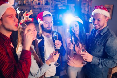 Arkadaşlar birlikte yeni yılı kutluyorlar. Arkadaşların İçkili Portresi Kokteyl Partisinin keyfini çıkarıyor. Gençler güler. Noel Baba şapkalı bir grup güzel genç insan. Bulanık Arkaplan.