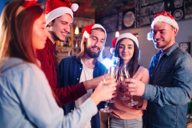Arkadaşlar birlikte yeni yılı kutluyorlar. Arkadaşların İçkili Portresi Kokteyl Partisinin keyfini çıkarıyor. Gençler güler. Noel Baba şapkalı bir grup güzel genç insan. Bulanık Arkaplan.