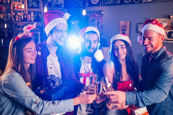 Friends celebrating new year\'s together. Portrait of Friends With Drinks Enjoying Cocktail Party. Young people laugh. Group of beautiful young people in Santa hats. Blur Background.