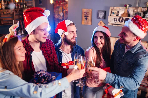 Friends celebrating new year's together. Portrait of Friends With Drinks Enjoying Cocktail Party. Young people laugh. Group of beautiful young people in Santa hats. Blur Background.