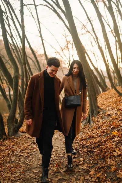 在一个美丽的秋天的森林里 一对时髦的年轻夫妇在户外 一对恋爱中的年轻夫妇在秋天的一天牵着手穿过一个公园 爱情和生活方式的概念 — 图库照片