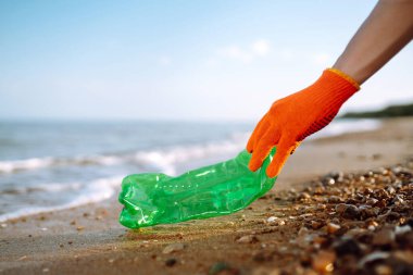 Erkekler plajda plastik şişe toplar. Koruyucu eldiven giyen gönüllü şişe plastiği topluyor. Deniz ve su kirliliği kavramı. Çevre koruma kavramı. 