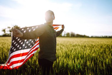 Amerikan bayrağını gururla sallayan genç bir adam. Vatansever, mavi gökyüzüne karşı ulusal Amerikan bayrağını göndere çekiyor. Bağımsızlık Günü, 4 Temmuz