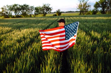 Amerikan bayrağını gururla sallayan genç bir adam. Vatansever, mavi gökyüzüne karşı ulusal Amerikan bayrağını göndere çekiyor. Bağımsızlık Günü, 4 Temmuz