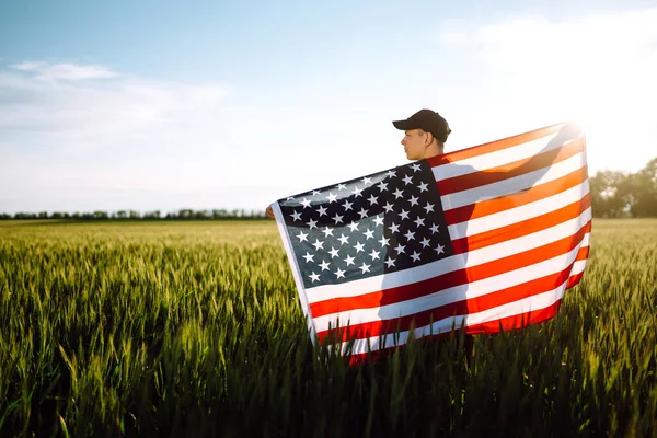 若い男は誇らしげにアメリカの旗を振って保持します 愛国者は青い空に国旗を掲揚する 独立記念日7月4日 — ストック写真