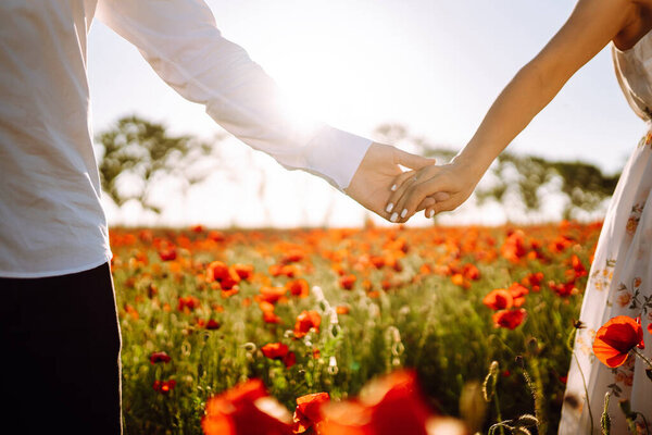 Holding hands of happy young couple having fun in poppy field. Love. Together. Beautiful sunset on a summer day.