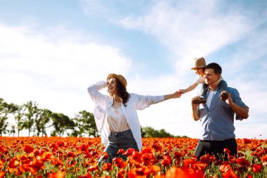 Haşhaş tarlasında yürüyen çocuklu bir aile. Anne, baba, küçük kız haşhaş tarlasında eğleniyor. Yaz zamanı..