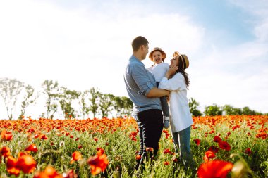 Haşhaş tarlasında yürüyen çocuklu bir aile. Anne, baba, küçük kız haşhaş tarlasında eğleniyor. Yaz zamanı..