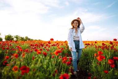 Şapkalı genç kız haşhaş tarlasında poz veriyor. Gün batımında haşhaş tarlasında yürüyen kıvırcık kız portresi. Yaz zamanı..
