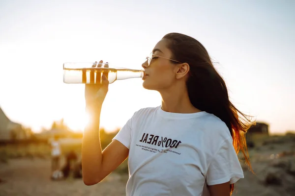 Young girl drinking beer from a bottle on the beach at sunset during  summer vacation. Summer holidays, relax and lifestyle concept.