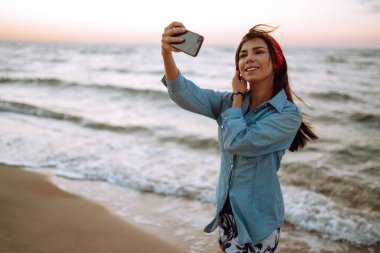 Güzel kız gün batımında sahilde selfie çeker. Rahatlama, seyahat ve yaz tatili konsepti.