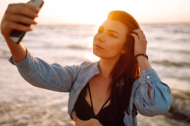 Güzel kız gün batımında sahilde selfie çeker. Rahatlama, seyahat ve yaz tatili konsepti.