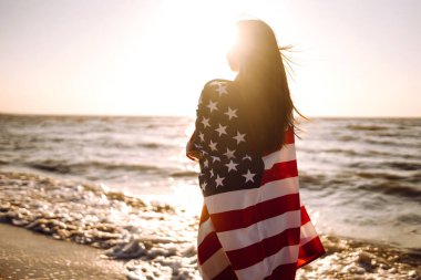 Gün batımında kumsalda Amerikan bayrağı taşıyan kız. 4 Temmuz. Bağımsızlık Günü. Vatansever bayram.