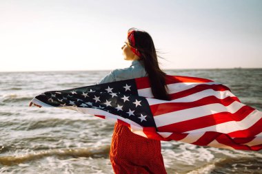 Gün batımında kumsalda Amerikan bayrağı taşıyan kız. 4 Temmuz. Bağımsızlık Günü. Vatansever bayram.