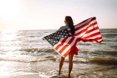 Gün batımında kumsalda Amerikan bayrağı taşıyan kız. 4 Temmuz. Bağımsızlık Günü. Vatansever bayram.