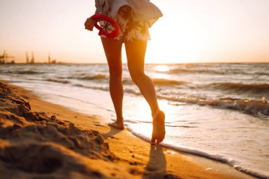 Gün batımında deniz kıyısında yürüyen kadın bacakları. Rahatlama, seyahat, özgürlük ve yaz tatili kavramı..