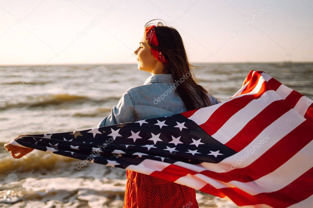 Girl with american flag on the beach at sunset. 4th of July. Independence Day. Patriotic holiday.