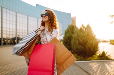 Alışveriş yapan bir kadın. Alışveriş yaptıktan sonra renkli alışveriş torbalarıyla şehirde dolaşan genç bir kız. Tüketim, satın alma, alışveriş, yaşam tarzı konsepti.