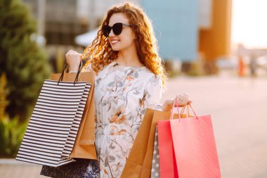 Alışveriş yapan bir kadın. Alışveriş yaptıktan sonra renkli alışveriş torbalarıyla şehirde dolaşan genç bir kız. Tüketim, satın alma, alışveriş, yaşam tarzı konsepti.