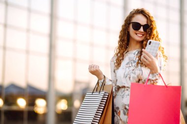 Alışveriş yapan bir kadın. Telefonu olan genç bir kız şehir caddesinde alışveriş yapıyor. Çevrimiçi alışveriş kavramı.