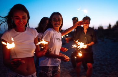 Bir grup genç, deniz kıyısında maytaplarla eğleniyor. İnsanlar plajda yeni yılı kutluyorlar. Plaj partisi, dinlenme, tatil.