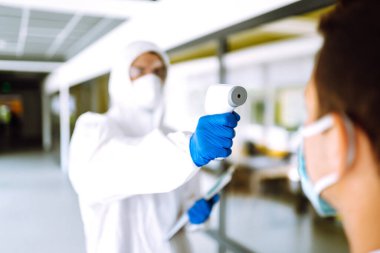 Hastalık kontrol uzmanı alnındaki sıcaklığı ölçmek için kızılötesi termometre cihazı kullanıyor. Covid-19, karantina veya virüs salgını kavramı.