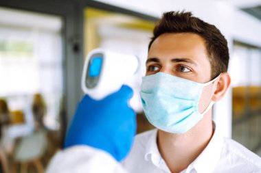 Ziyaretçiler alında kızılötesi dijital termometre ile ateş ölçümü yapmak zorundalar. Covid-19, karantina veya virüs salgını kavramı.