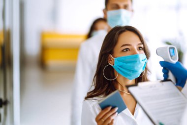 Eldivenle termometreyi tut. Tıbbi ofis ölçüm ürünü. Hastalık kontrol uzmanı alnındaki sıcaklığı ölçmek için kızılötesi termometre cihazı kullanıyor. Covid 19.