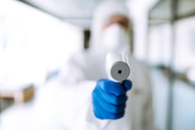 Ofisteki sıcaklığı kontrol etmek için kızılötesi termometre cihazlı bir hastalık kontrol uzmanı. Salgının yayılmasını önleme ve koronavirüsü tedavi etme kavramı karantinada salgındır. 