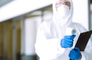 Ofisteki sıcaklığı kontrol etmek için kızılötesi termometre cihazlı bir hastalık kontrol uzmanı. Salgının yayılmasını önleme ve koronavirüsü tedavi etme kavramı karantinada salgındır. 