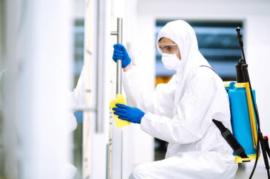 COVID-19 'u önlemek için ofisi temizleme ve dezenfekte etme. Koruyucu takım elbiseli ve maskeli bir dezenfektan ofis mobilyası dezenfektanlarını yıkıyor. Yüzeyleri olan zatürree virüsünün yayılmasını önlemek.