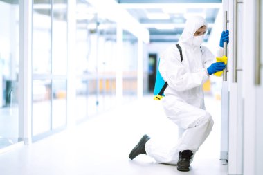 COVID-19 'u önlemek için ofisi temizleme ve dezenfekte etme. Koruyucu takım elbiseli ve maskeli bir dezenfektan ofis mobilyası dezenfektanlarını yıkıyor. Yüzeyleri olan zatürree virüsünün yayılmasını önlemek.