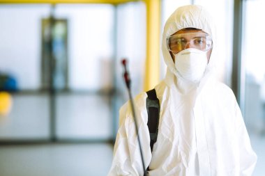 COVID-19 koronavirüs için müteahhit dezenfekte ofisi. Koruyucu giysili ve maskeli bir dezenfektan ofiste dezenfektan sıkar. Yüzeyleri olan zatürree virüsünün yayılmasını önlemek.