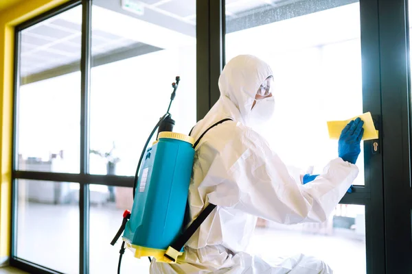 Cleaning and disinfection of office to prevent COVID-19. A disinfector man in a protective suit and mask washes office furniture disinfectants. Prevention of spreading pneumonia virus with surfaces.