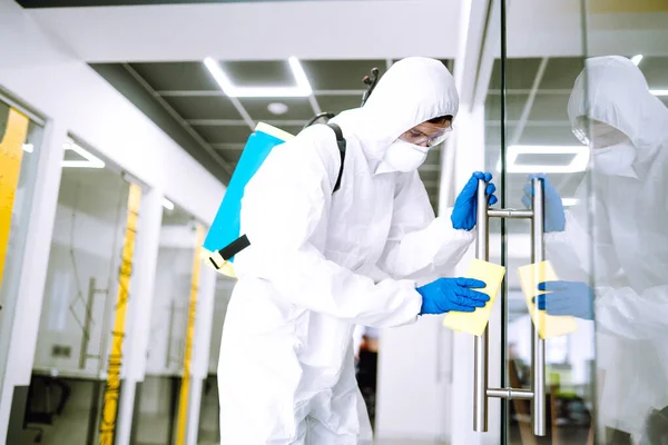 Cleaning and disinfection of office to prevent COVID-19. A disinfector man in a protective suit and mask washes office furniture disinfectants. Prevention of spreading pneumonia virus with surfaces.