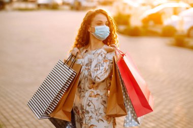 Alışveriş sonrası paketleri olan steril tıbbi maskeli güzel bir kız. Karantina şehrinde alışveriş. Covid 2019.