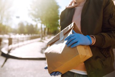 Koruyucu maskeli bir kurye içinde yiyecek olan kağıt paketleri teslim eder. Teslimat karantina altında. Salgın. Covid 2019.