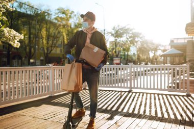 Koruyucu maskeli bir kurye içinde yiyecek olan kağıt paketleri teslim eder. Teslimat karantina altında. Salgın. Covid 2019.