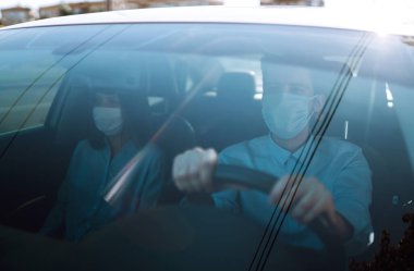 Coronavirus karantinası sırasında tıbbi maskelerle araba süren genç bir adam ve kadın. Güvenli taksi, virüsten korunma. Covid 2019.