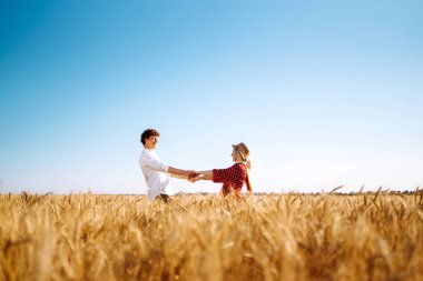 Bir çift buğday tarlasında eğleniyor ve dinleniyor. Genç kız arkadaş ve erkek arkadaş öpüşüyor ve sarılıyorlar. Gençlik, aşk ve yaşam tarzı kavramı.