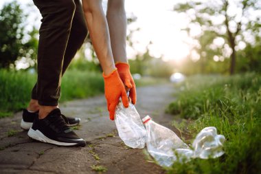 Parkta boş plastik şişeler. Parkta çöp toplama. Koruyucu eldiven giyen erkekler şişe plastiği toplar. Doğayı kurtar.